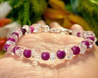 May include: A bracelet made with clear and pink faceted gemstone beads. The bracelet is on a person's wrist.