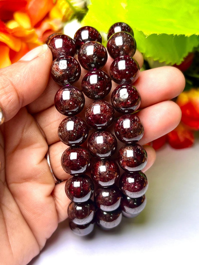 May include: Three red garnet gemstone bracelets with round beads. The bracelets are stacked on top of each other and are being held in a hand.
