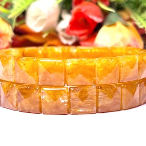 May include: A double-strand bracelet made of square-shaped, golden yellow beads. The beads have a shimmery, almost metallic, finish.