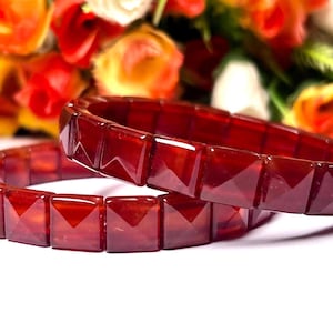 May include: Two red carnelian gemstone bracelets with square-shaped beads. The bracelets are stacked on top of each other.