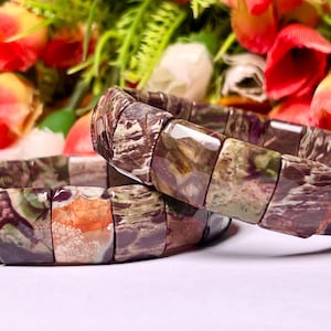 Puede incluir: Dos pulseras hechas con cuentas de piedra con patrones marrones, verdes y naranjas. Las pulseras están apiladas una encima de la otra.