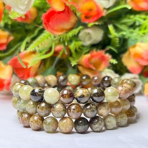 May include: Three stacked bracelets made of green and brown gemstone beads. The beads are round and have a speckled appearance.