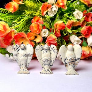 May include: Three white and black speckled stone angel figurines. The angels are carved in a standing pose with wings outstretched.