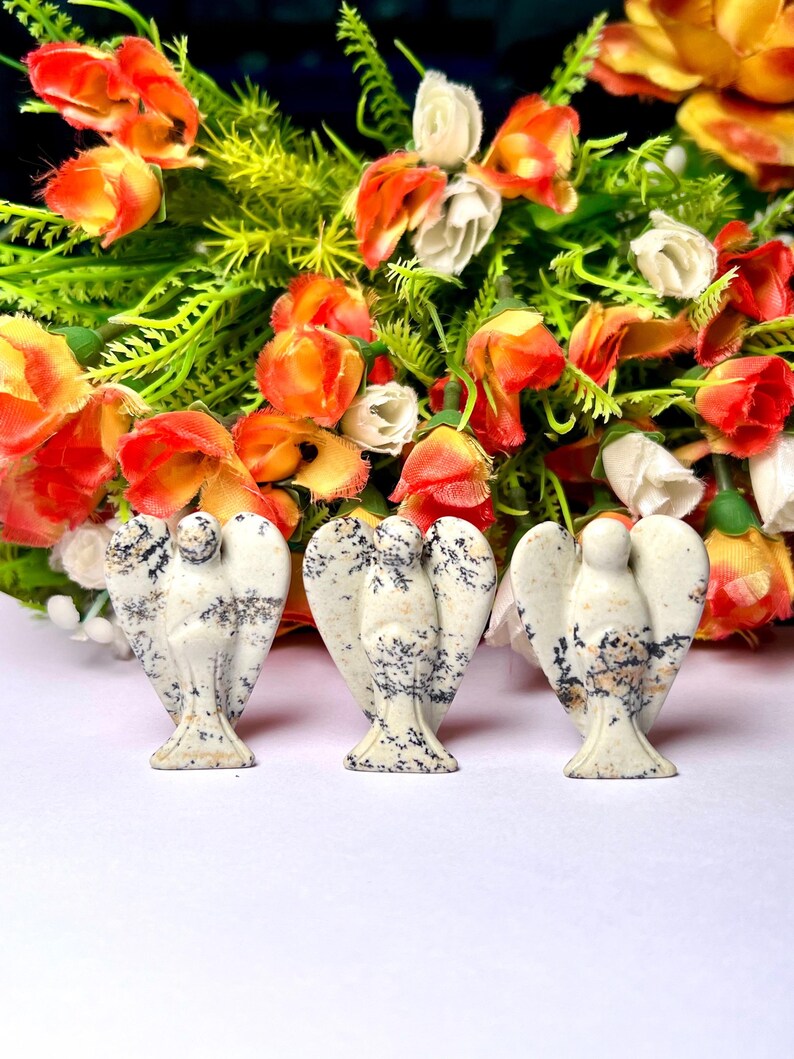 May include: Three white and black speckled stone angel figurines. The angels are carved in a standing pose with wings outstretched.