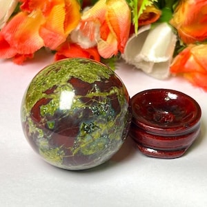 May include: A green, red, and brown sphere made of polished stone sits on a wooden stand. The sphere is about 2 inches in diameter.