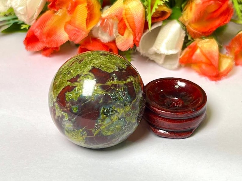 May include: A green, red, and brown sphere made of polished stone sits on a wooden stand. The sphere is about 2 inches in diameter.