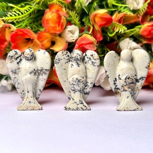May include: Three white and black speckled stone angel figurines. The angels are carved in a simple, minimalist style with wings outstretched.