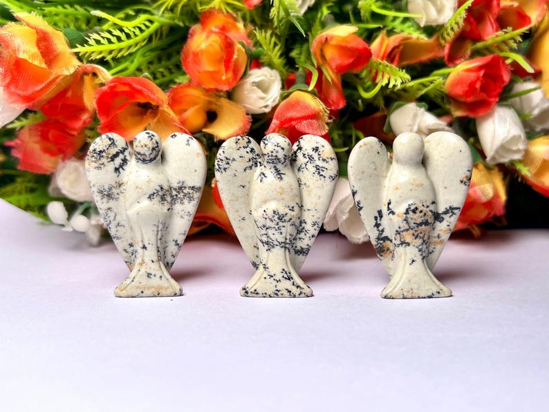 May include: Three white and black speckled stone angel figurines. The angels are carved in a simple, minimalist style with wings outstretched.