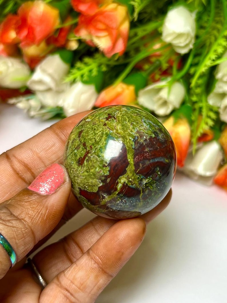 May include: Green and red jasper sphere, polished and smooth, with a swirling pattern of green, red, and brown. The sphere is about the size of a golf ball.