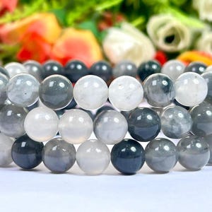 Puede incluir: Un brazalete hecho de cuentas de piedras preciosas grises y blancas. Las cuentas son redondas y tienen un acabado liso y pulido.