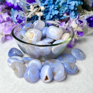 May include: A bowl filled with blue lace agate tumbled stones. The stones are smooth and polished, with a variety of blue and white patterns.