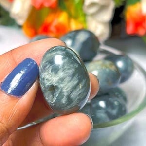 May include: A close-up of a smooth, oval-shaped blue and gray gemstone. The gemstone has a swirling pattern and a glossy finish.