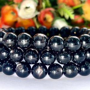 May include: A black gemstone bracelet with multiple strands of round beads. The beads are shiny and have a slight sparkle.