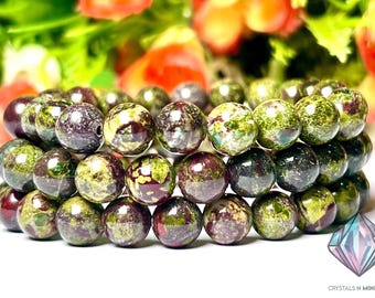 May include: A close-up of a multi-strand bracelet made of green, brown, and red speckled beads. The beads are round and have a natural, earthy look.