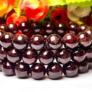 May include: A bracelet made of dark red garnet beads. The beads are round and have a smooth, polished finish. The bracelet is stacked with multiple rows of beads.