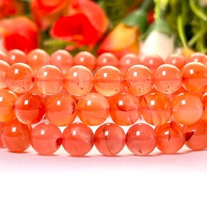 May include: Three stacked bracelets made of orange carnelian beads. The beads are round and have a translucent appearance.