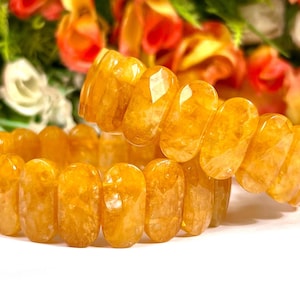 Puede incluir: Dos pulseras de piedras amarillas hechas con cuentas ovaladas. Las pulseras están apiladas una encima de la otra.