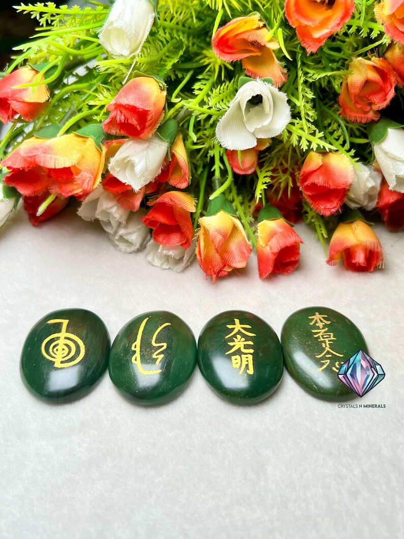 May include: Four green oval-shaped stones with gold Chinese characters inscribed on them. The stones are arranged in a row from left to right. The characters are "身", "心", "光明", and "本質".