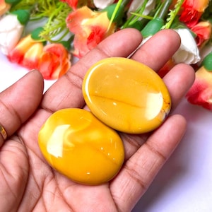 May include: Two yellow and orange polished stones, also known as palm stones, in the shape of an oval. The stones are smooth and have a glossy finish.