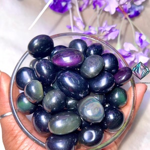 May include: A bowl of tumbled obsidian stones with iridescent green and purple hues. The stones are smooth and polished, and they have a dark, almost black, color.