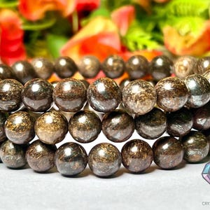 Puede incluir: Un brazalete de triple hebra hecho de cuentas redondas de piedra preciosa de color marrón oscuro. Las cuentas tienen un acabado moteado e iridiscente.