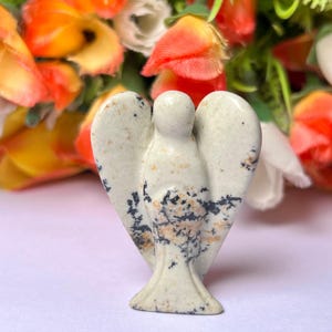 May include: A white and black speckled stone angel figurine. The angel has a rounded head and outstretched wings.