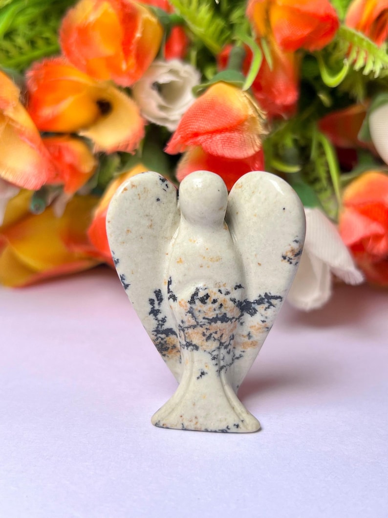 May include: A white and black speckled stone angel figurine. The angel has a rounded head and outstretched wings.
