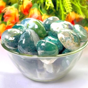 May include: A bowl filled with green moss agate tumbled stones. The stones are smooth and polished, with a variety of green and white patterns.