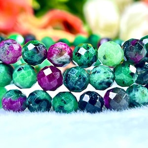 Op de afbeelding: Een close-up van een meerstrengige armband gemaakt van gefacetteerde groene en paarse edelsteen kralen. De kralen zijn rond en hebben een gepolijste afwerking.