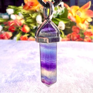 May include: A silver pendant with a purple and white fluorite crystal point. The crystal is set in a silver bezel and hangs from a silver chain.