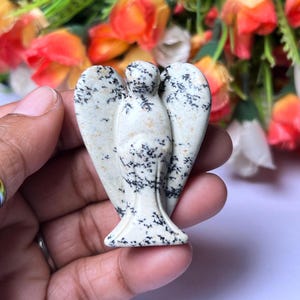 May include: A white and black speckled stone angel figurine. The angel has wings and a detailed face.
