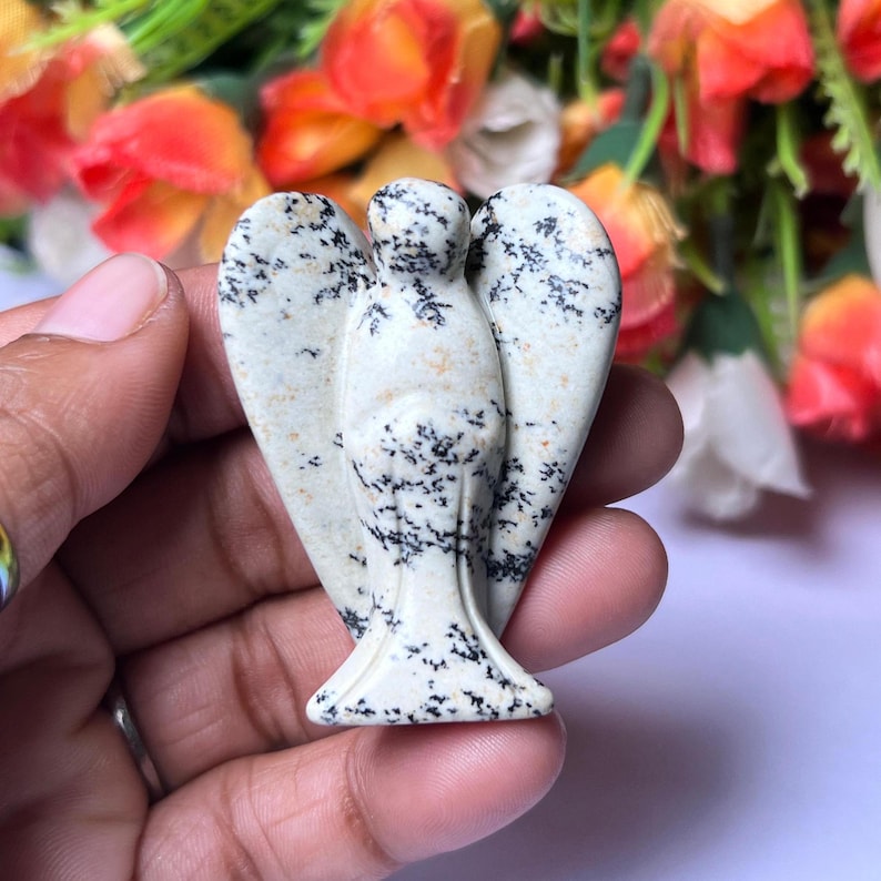 May include: A white and black speckled stone angel figurine. The angel has wings and a detailed face.