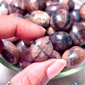 May include: A bowl filled with tumbled, polished, dark red and black star-shaped stones. The stones have a natural, rough texture and a shiny, polished finish.