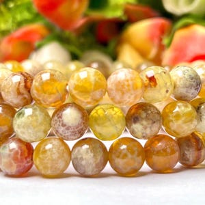 Peut inclure: Un bracelet multi-rangs composé de perles rondes en agate jaune avec des motifs blancs et bruns. Les perles sont polies et ont une finition lisse et brillante.