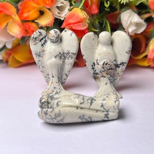 May include: Three white and black speckled stone angel figurines. The angels are carved in a standing pose with wings outstretched.
