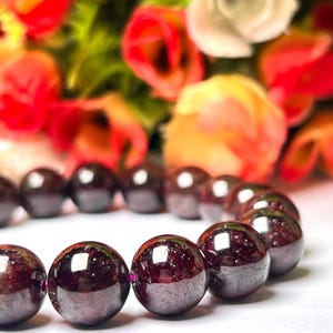 May include: A bracelet made of dark red gemstone beads. The beads are round and polished, and they have a slight shine. The bracelet is strung on a thin, clear string.