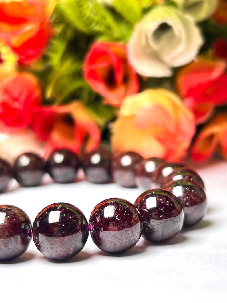 May include: A bracelet made of dark red gemstone beads. The beads are round and polished, and they have a slight shine. The bracelet is strung on a thin, clear string.