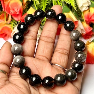 Pode incluir: Um bracelete de pedras preciosas pretas e cinzas com contas redondas. O bracelete é feito de obsidiana e pedra da lua.