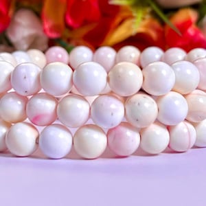 May include: A bracelet made of white and pink shell beads. The beads are round and have a smooth, polished finish.