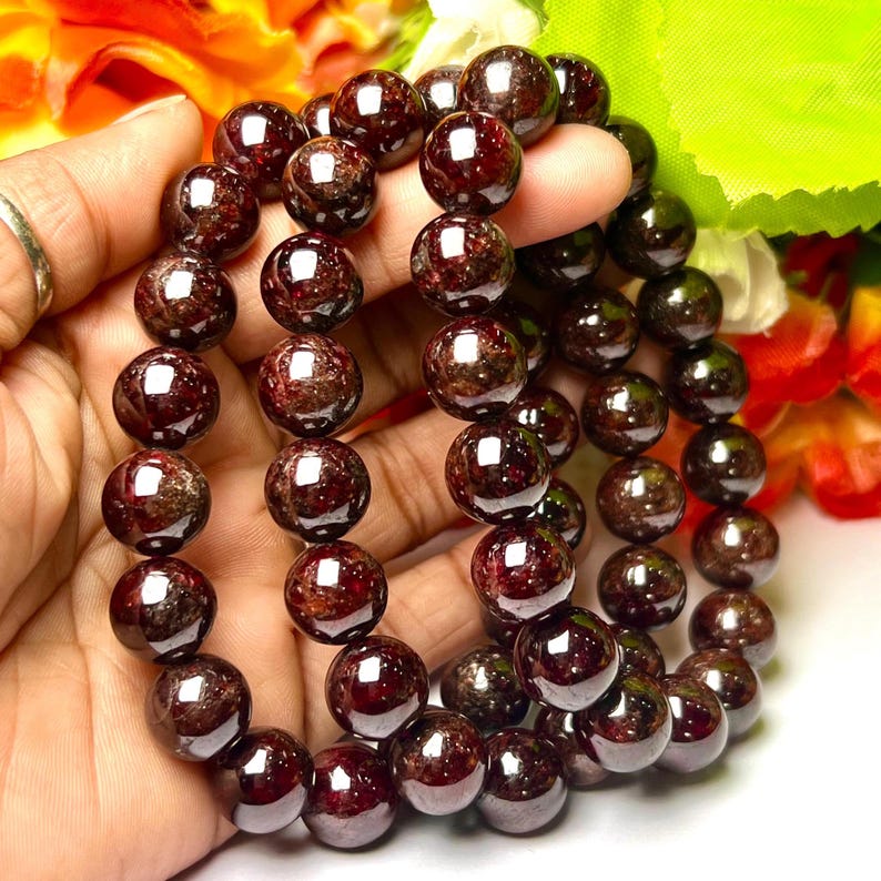 May include: A bracelet made of dark red garnet beads. The beads are round and have a smooth, polished finish.