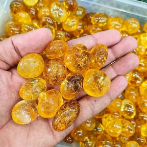 May include: A collection of tumbled citrine stones, each with a smooth, polished surface and a warm, golden yellow color. The stones are arranged in a hand, showcasing their natural beauty and unique shapes.