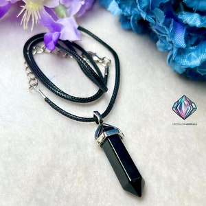 Puede incluir: Collar con colgante de punta de obsidiana negra con engaste plateado en un cord&oacute;n negro. Crystals N Minerals est&aacute; impreso en la imagen.
