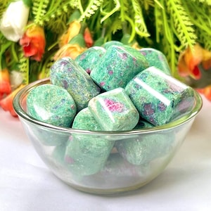 May include: A bowl filled with green and pink tumbled stones. The stones are smooth and have a speckled appearance.