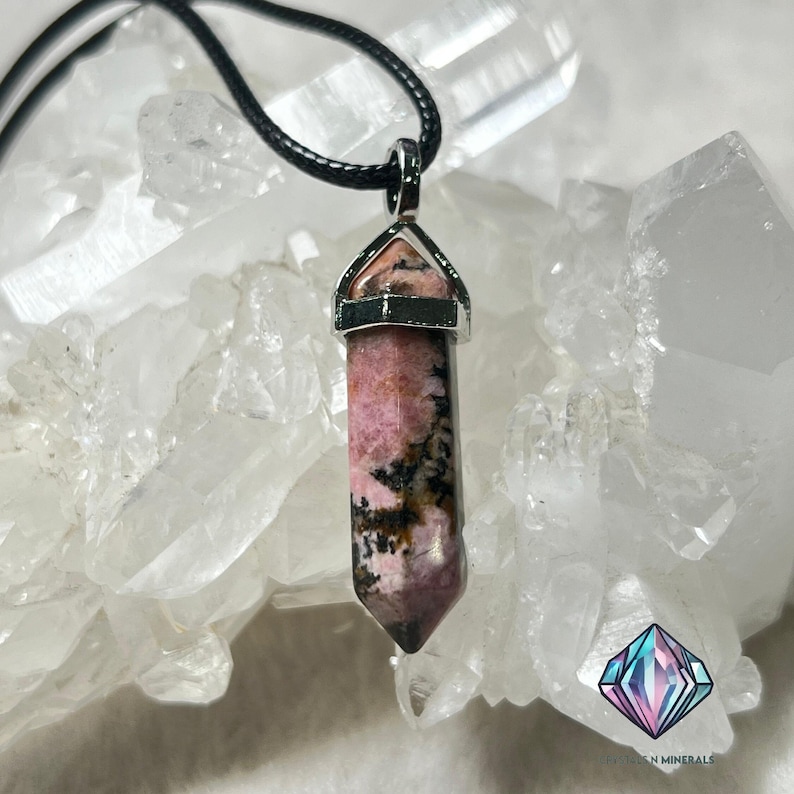 May include: A pink and black crystal pendant on a black cord necklace. The pendant is a point shape with a silver setting. The crystal is surrounded by white quartz crystals.