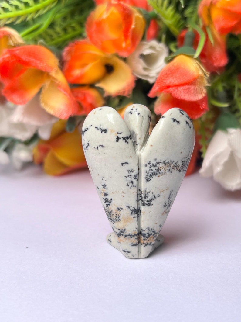 May include: White and black speckled stone angel figurine. The angel is carved in a standing position with wings outstretched.