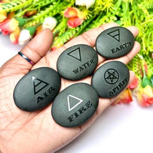 May include: Five smooth, black stones with different symbols and the words "Air", "Water", "Earth", "Spirit", and "Fire" engraved on them.