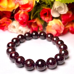 May include: A dark red garnet gemstone bracelet with round beads. The bracelet is on a white surface.