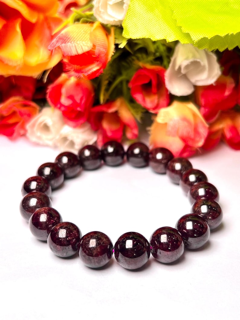 May include: A dark red garnet gemstone bracelet with round beads. The bracelet is on a white surface.