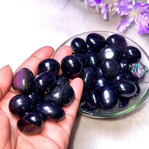 May include: A collection of black obsidian tumbled stones, also known as black glass, in a small bowl. The stones are smooth and polished, with a shiny, iridescent finish.