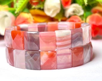 May include: A pink and orange agate stone bracelet with square-shaped beads. The bracelet is made of natural stones and has a unique pattern.